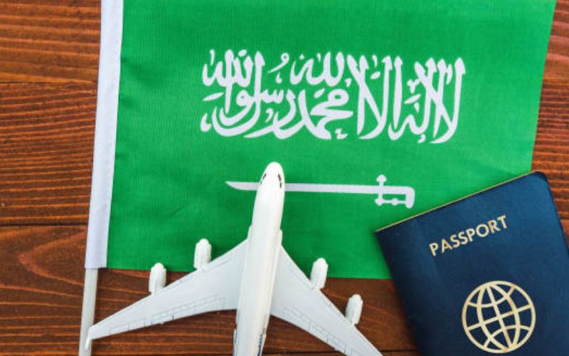 Saudi flag with a passport and toy airplane on a wooden surface.