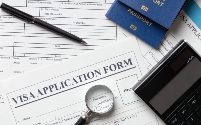 Visa application form with passports, pen, calculator, and magnifying glass on a desk