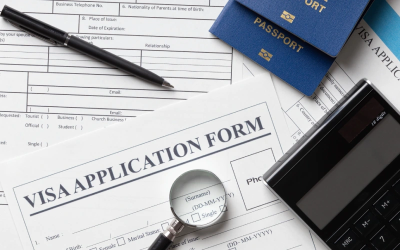 Visa application form with passports, pen, calculator, and magnifying glass on a desk